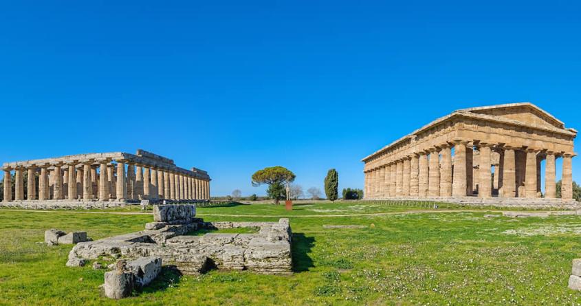 Templi antichi a Paestum, immersi in un paesaggio verde e cielo azzurro.